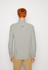 Ljusgrå långärmad skjorta i linne med krage. Har en broderad logotyp i röd, vit och blå på övre ryggen.