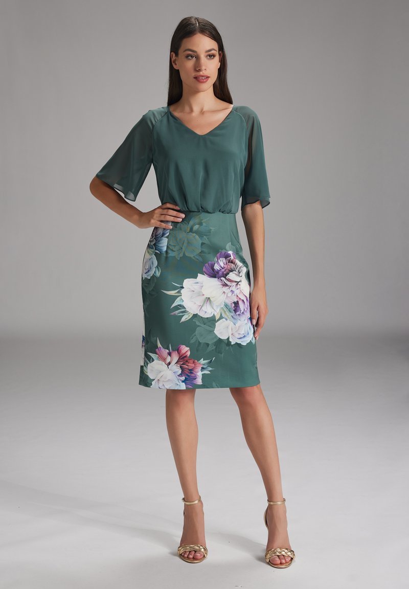 Robe à manches courtes et décolleté en V de couleur verte avec un motif floral. La partie inférieure présente de grandes fleurs dans des tons de violet et de rose.