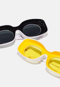Dos pares de gafas de sol: uno con lentes negros y un marco negro, el otro con lentes amarillos y un marco amarillo; ambos presentan detalles blancos.