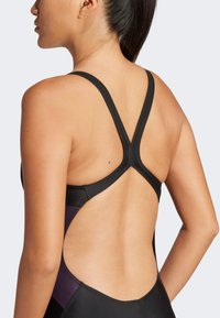Schwarze und lila Badeanzug mit Racerback-Design, kontrastierenden Trägerschlaufen und geöffnetem Rücken für verbesserte Beweglichkeit.