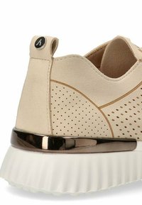 Zapatillas de ante beige con patrones perforados, un acento de bronce suave alrededor de la suela y una suela exterior de goma blanca texturizada.