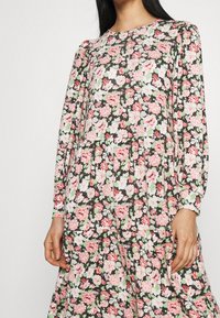 Robe florale à manches longues ; fond noir avec des fleurs roses et blanches. Ourlet volé et texture douce. Encolure ronde.