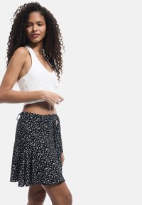 Jupe noire à fleurs blanches, design plissé, lien sur le côté, tissu léger. Top ajusté blanc, sans manches, style cropped.
