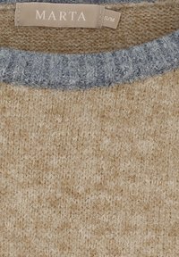 Tansfarvet og grå strikket sweaterkrave med et beige stofmærke, der står "MARTA" og størrelsesmærkaten "S/M" syet indeni.