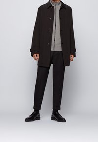 Svart knäppa-kappor, grå zip-up jacka, svarta byxor och svarta skor. Slät tyg, avslappnad passform, med uppvikta ärmar på byxorna.