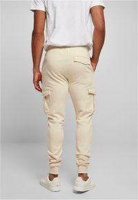 Beige cargo joggers made of soft material, featuring side pockets and ribbed cuffs. Worn with a white t-shirt and white sneakers.