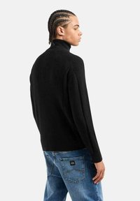 Maglione nero a collo alto con texture a coste, maniche lunghe e vestibilità rilassata, abbinato a jeans in denim blu con tasche posteriori.