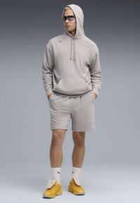 Gray hoodie with a front pocket and logo, paired with matching shorts. Yellow sneakers and sunglasses complete the look.