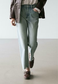 Hellblaue, hoch taillierte Jeans aus Denim mit lockerem Schnitt und ausgefransten Saumdetails. Kombiniert mit braunen Mokassin-Schuhen.