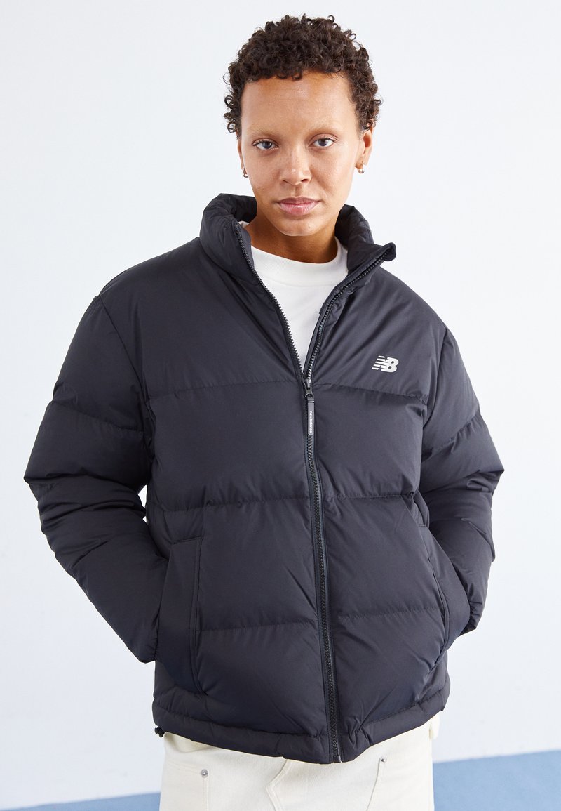 Schwarze Steppjacke mit Reißverschluss, hohem Kragen und gestepptem Design. Verfügt über ein kleines Logo auf der Brust und Taschen vorne.