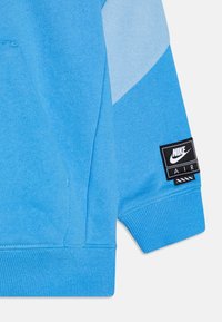 Blauer Nike Air Sweatshirt-Ärmel mit schwarzem und weißem Nike Air-Logo-Patch am gerippten Bund, mit hellblauen und mittelblauen Farbkombinationen.