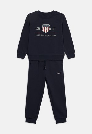 Marineblauw sweatshirt- en joggingbroekset met GANT-logo en schildembleem in rood, wit en grijs op de voorkant van het sweatshirt, met elastische boorden en tailleband.