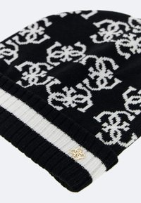 Berretto a maglia in bianco e nero con un motivo ripetuto, texture a coste e dettaglio del logo dorato. Design arrotolato per maggiore calore.