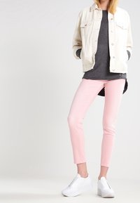 Veste en denim clair, t-shirt gris, jeans skinny roses et baskets blanches. Tissu lisse avec une coupe décontractée ; peu de détails.