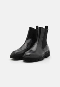 Botas Chelsea de cuero negro con paneles elásticos laterales, suela de goma gruesa y lengüetas para facilitar el calzado. Textura suave y diseño de punta redonda.