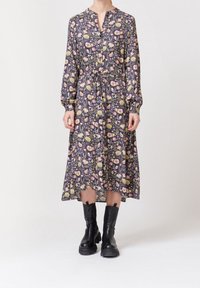 Robe midi à imprimé floral de couleur violet foncé avec manches longues, boutonnée sur le devant, ceinture à nouer à la taille et jupe fluide, associée à des bottines noires.