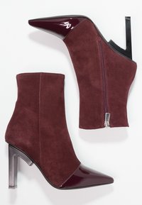 Bottines bordeaux à bout pointu ; en suède avec des accents en cuir verni. Dotées d'une fermeture éclair et d'un talon aiguille élégant.