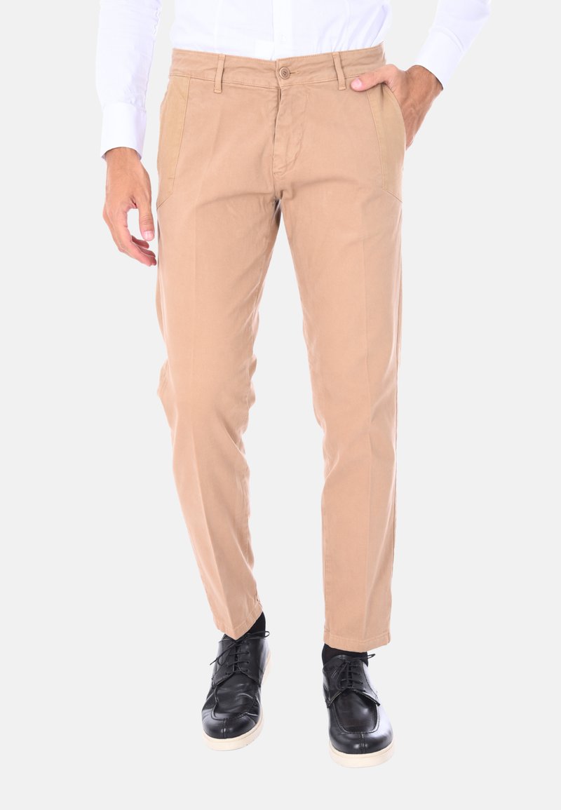 Pantaloni chinos beige in cotone con vestibilità slim, dotati di tasche laterali, chiusura con bottone e abbinati a scarpe nere stringate.
