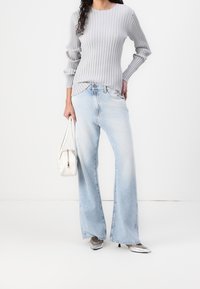Jeans de pierna ancha azul claro combinados con una blusa gris de manga larga con canalé. El conjunto se complementa con un bolso blanco y zapatos plateados.