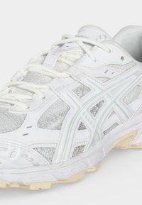 White athletic sneaker with mesh panels, synthetic overlays, and beige rubber sole shown from a side close-up angle.