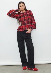 Blusa a quadri rossa con corpetto arricciato e maniche ampie, abbinata a pantaloni neri a gamba larga e scarpe rosse con dettagli bianchi.