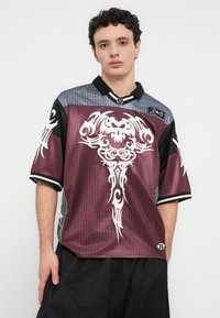 Πόλο μπλούζα με κοντά μανίκια σε μπορντό και γκρι, με μαύρες λεπτομέρειες και λευκό φυλετικό σχέδιο. Κατασκευασμένη από ομαλό, ελαφρύ ύφασμα.