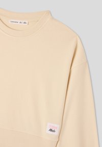 Felpa beige chiaro con colletto e polsini a coste. Presenta un'etichetta bianca con "STREET" in rosa e "Mode" in nero sul lato.