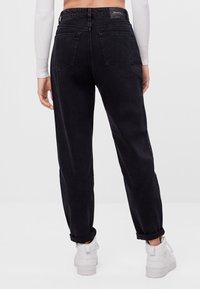 Jeans de mezclilla negra con un corte relajado, puños enrollados, bolsillos traseros y una etiqueta de la marca visible en la cinturilla. Textura suave.