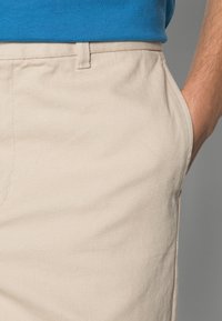 Chinos beige testurizzati con taglio dritto, dotati di tasche frontali e un motivo a trama sottile, abbinati a una camicia blu in vita.