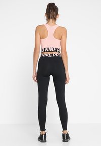 Top de sport rose à la coupe courte avec un dos nageur, associé à un legging noir avec une taille élastique et une marque audacieuse. Tissu lisse et extensible.