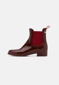 Botas de lluvia burdeos con un acabado brillante y resistente al agua, paneles laterales elásticos y una lengüeta. Presentan un tacón bajo y acentos texturizados.