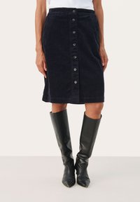 Sötétkék kord midi szoknya gombos elülső záróval, textúrált felülettel és egyenes szabással. Fekete, magas bőr csizmával párosítva.