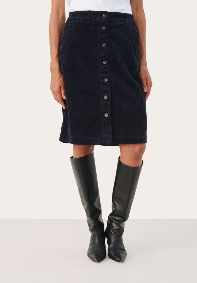 Sötétkék kord midi szoknya gombos elülső záróval, textúrált felülettel és egyenes szabással. Fekete, magas bőr csizmával párosítva.
