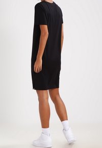 Svart kortärmad klänning med avslappnad passform, sidofickor och mjuk textur. Kombinerad med vita sneakers och ankelsockar.