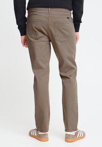 Szaro-brązowe spodnie slim fit z pięcioma kieszeniami i naszyciami z tyłu, w połączeniu z brązowymi sneakersami z białymi paskami.