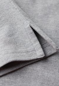 Nahaufnahme eines hellgrauen Stoffes mit umgeschlagenem Saum und seitlichem Schlitz, der strukturierte Strick- und Nähdetails zeigt.