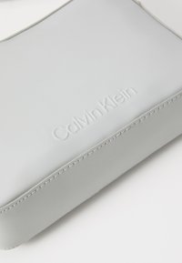 Pochette in pelle grigia Calvin Klein con logo impresso, texture liscia, linee pulite e cuciture a contrasto lungo i bordi.
