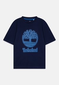 Camiseta de algodón azul marino con mangas cortas, que presenta un logo de árbol azul y el texto "Timberland" centrado debajo del gráfico.