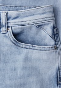 Poche d'un jean en denim bleu clair avec passants de ceinture visibles, rivets métalliques et détails de couture sur la texture du tissu.