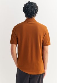 Ruda trumpomis rankovėmis polo marškinėliai, švelnaus tekstūros, šiek tiek pailginta nugara, plokščias apykaklė ir rankovių manžetai.