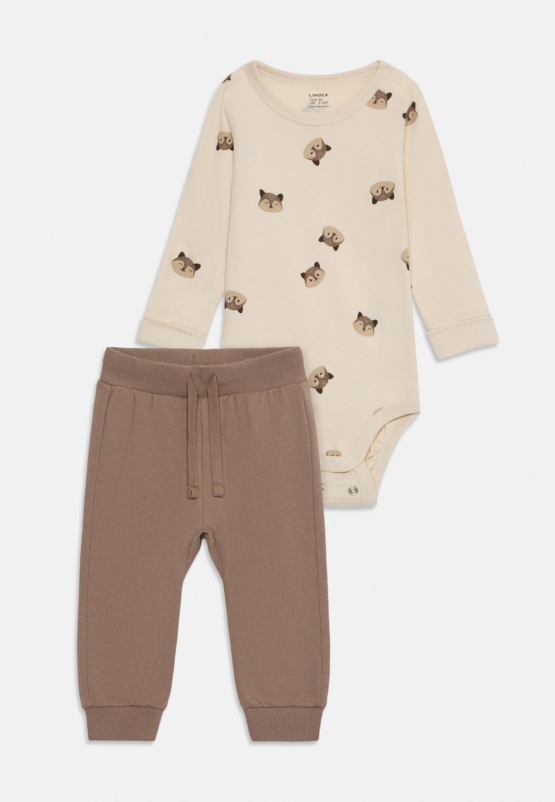 Kremno dolgi bodi z dolgimi rokavi z živalskim vzorcem in pritrdilnimi gumbi, v kombinaciji s toplimi hlačami v rjavi barvi, ki imajo elastičen pas in manšete.