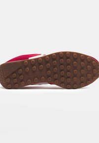 Suola di scarpa da corsa in suede rosso con fondo in gomma marrone caratterizzato da motivi circolari; dettagli del logo bianco vicino al tallone.
