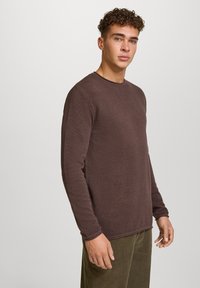 Brązowa, strukturalna bluzka z długim rękawem i okrągłym dekoltem. Charakteryzuje się subtelnym wzorem i luźnym krojem. Połączona z oliwkowymi spodniami.