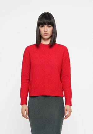 Red woolen sweater with a ribbed neckline and cuffs, featuring a straight cut and a slightly cropped length. Worn with a dark pencil skirt.