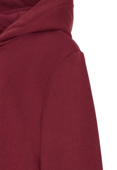 Primo piano di un cappuccio in tessuto bordeaux e della cucitura della spalla di una felpa o di un hoodie su uno sfondo bianco.