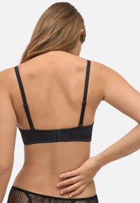 Sostenedor negro con tirantes delgados ajustables, tela suave, cierre de gancho y ojo en la parte posterior, y un diseño minimalista sin adornos.
