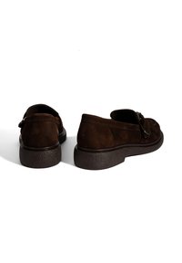 Braune Wildlederschuhe mit runder Spitze und einer niedrigen strukturierten Gummisohle. Verfügen über eine dekorative Schnalle an der Seite.