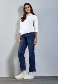 Vit skjorta med knappar och långärmar, kombinerad med mörkblå raka jeans och vita högskurna sneakers. Slät tygstruktur.