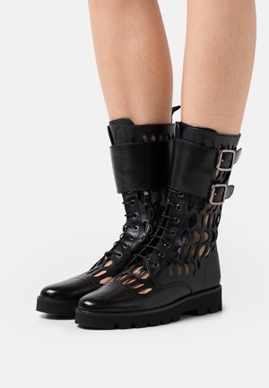 Svarta läderankelboots med en urklippt design, slät yta, snörning, två spännelement och en kraftig sula.