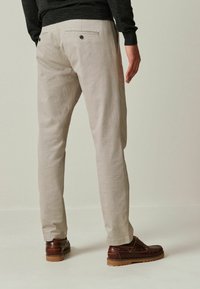 Lys beige teksturerede bukser med slim fit, der har to baglommer med sorte knapper og er parret med brune sko.